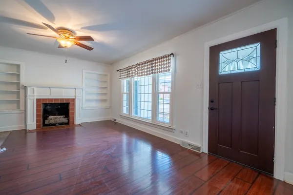 an empty room with wooden floor a chandelier fan and windows