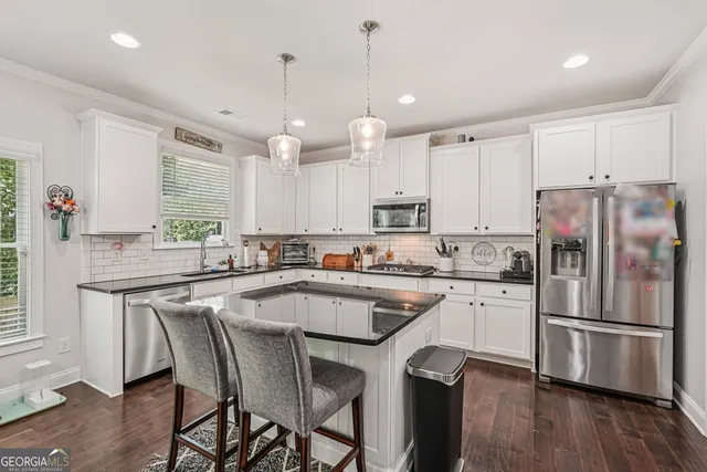 a kitchen with stainless steel appliances granite countertop a refrigerator a sink dishwasher a stove and white cabinets with wooden floor