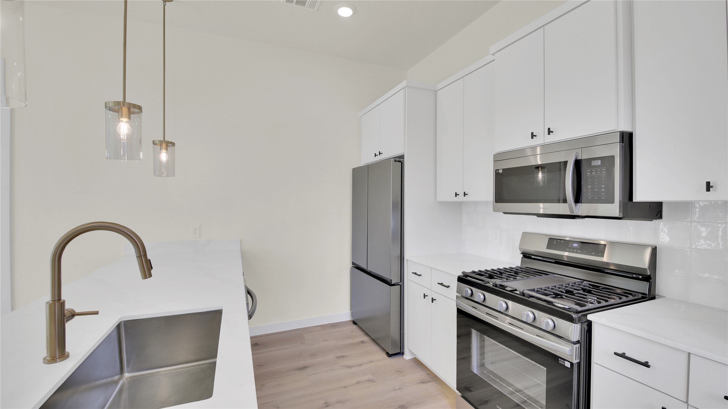 6802 Montana Street, Unit 1 Austin, TX 78741 - Photo 6 of 20 Kitchen with stainless steel appliances, hanging light fixtures, white cabinets, light wood-style flooring, and light stone counters