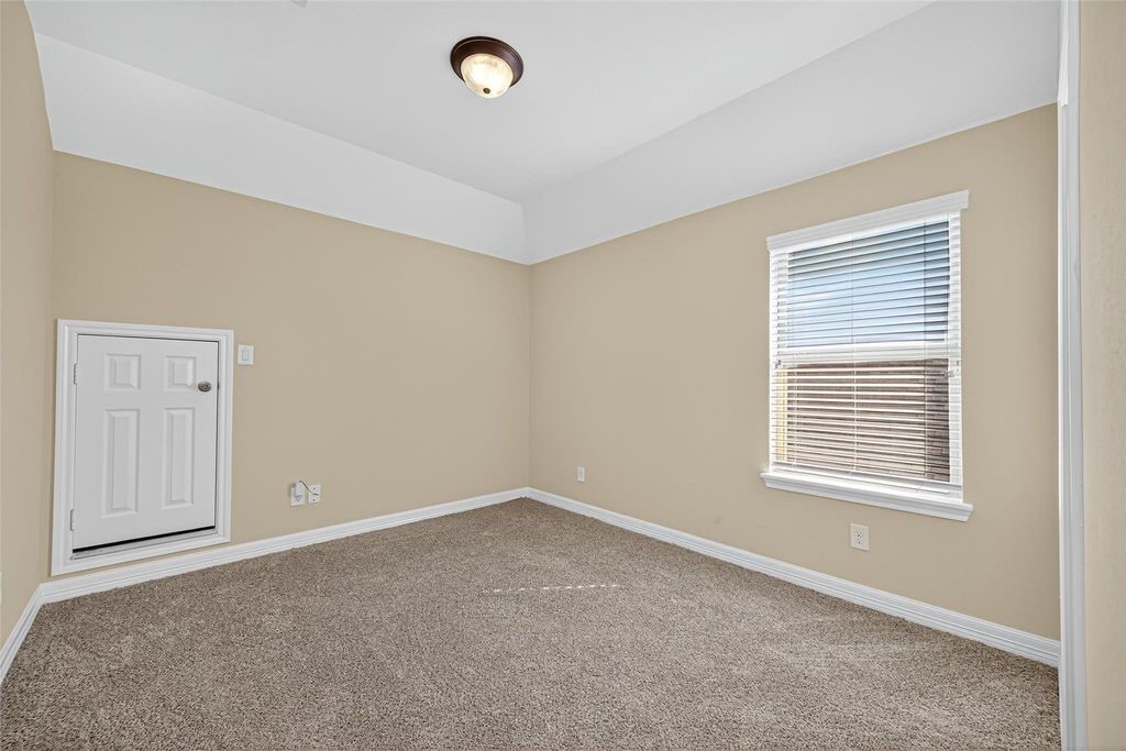 22743 Adrift Row Lane Porter, TX 77365 - Photo 20 of 33 This room features neutral-colored walls, a carpeted floor, and a window with blinds providing natural light. It includes a small door, likely for storage, and a ceiling light fixture.