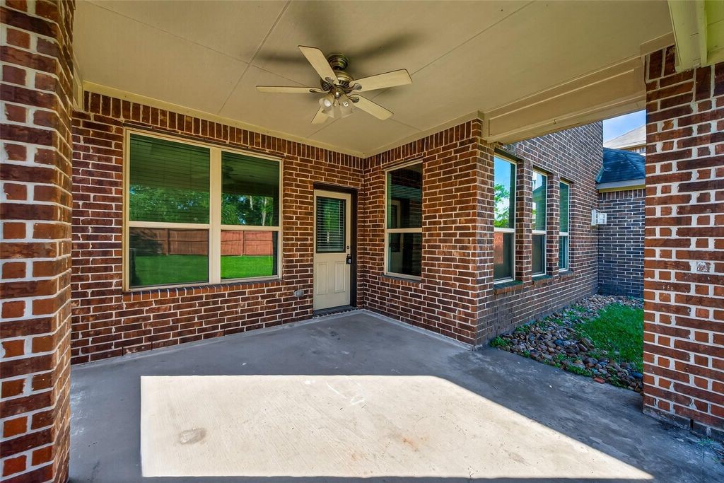 22743 Adrift Row Lane Porter, TX 77365 - Photo 31 of 33 Spacious covered patio with a ceiling fan, surrounded by red brick walls and large windows, offering a view of the backyard. Perfect for outdoor relaxation and entertaining.