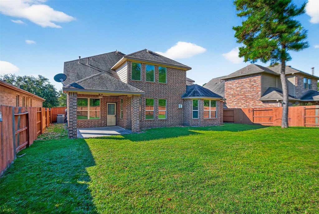 22743 Adrift Row Lane Porter, TX 77365 - Photo 33 of 33 This spacious two-story brick home features a large backyard with a well-maintained lawn, a covered patio, and is enclosed by a wooden fence, offering privacy and ample outdoor space.