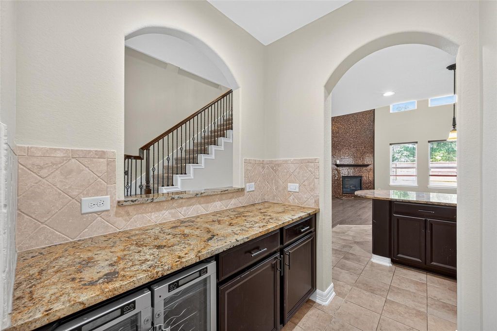 22743 Adrift Row Lane Porter, TX 77365 - Photo 8 of 33 This photo showcases a modern kitchen area with granite countertops, arched entryways, and a wine cooler. It opens to a living room with large windows and a fireplace, offering a spacious, open-concept feel.