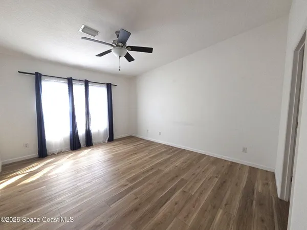 an empty room with wooden floor fan and windows