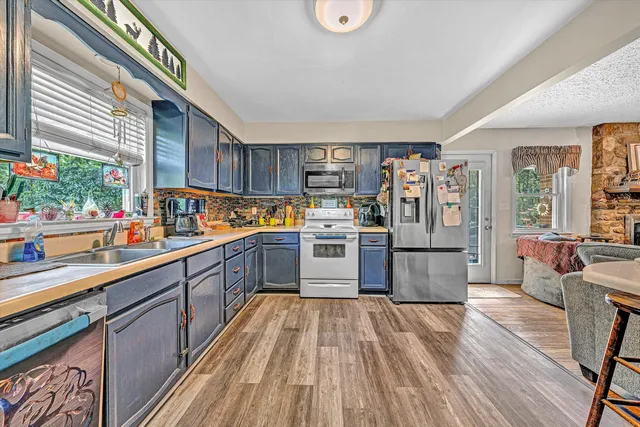 a kitchen with stainless steel appliances granite countertop a refrigerator a sink dishwasher a stove and white countertops with wooden floor