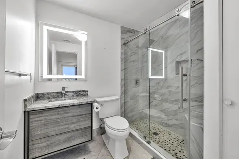 a bathroom with a granite countertop toilet a sink a mirror and shower