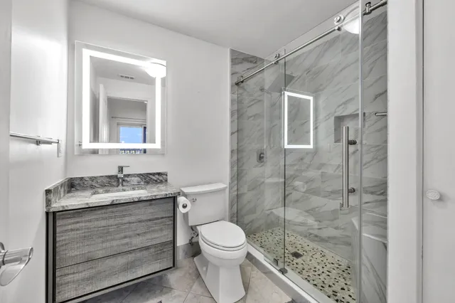 a bathroom with a granite countertop toilet a sink a mirror and shower