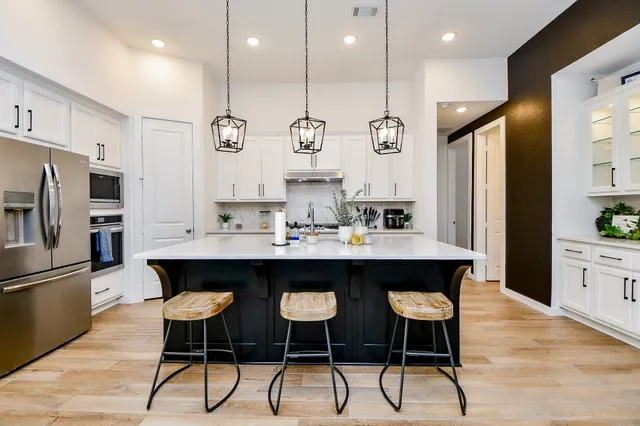 a kitchen with stainless steel appliances kitchen island granite countertop a sink a refrigerator and white cabinets with wooden floor