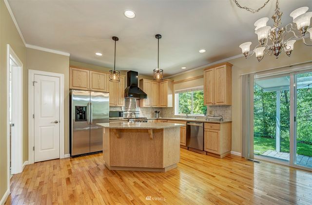 a kitchen with stainless steel appliances granite countertop a refrigerator a sink dishwasher a stove and a large window with wooden floor