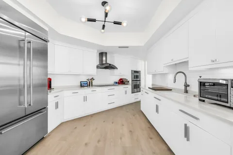 a large kitchen with stainless steel appliances granite countertop a refrigerator a stove a sink dishwasher and white cabinets with wooden floor