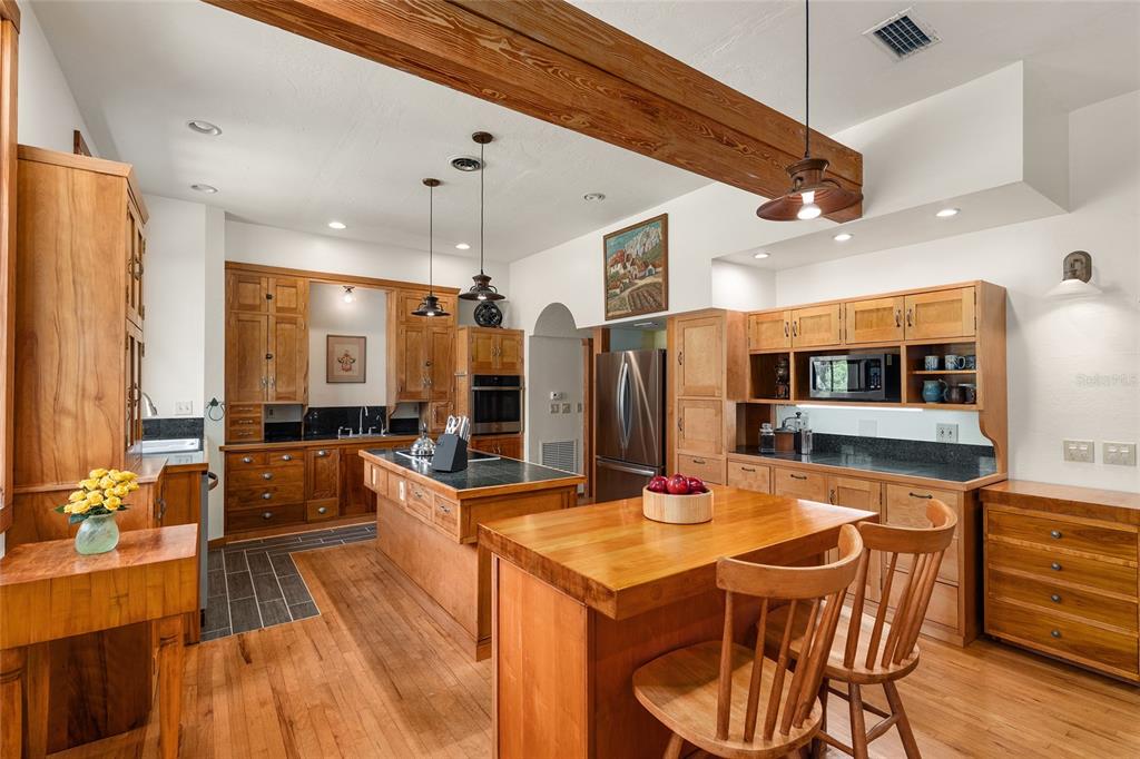 21736 Northwest 75th Avenue Road Micanopy, FL 32667 - Photo 27 of 88 a kitchen with stainless steel appliances kitchen island granite countertop a table chairs in it and wooden floors
