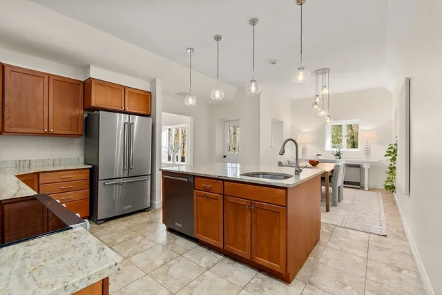 a kitchen with stainless steel appliances granite countertop a refrigerator a sink dishwasher a oven and a dining table with wooden floor