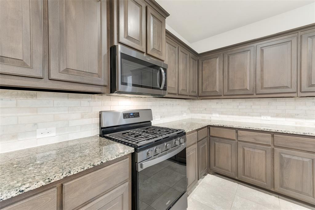 1419 Fox Hollow Road Krum, TX 76249 - Photo 11 of 29 Kitchen with stainless steel appliances, light stone counters, light tile patterned floors, and decorative backsplash