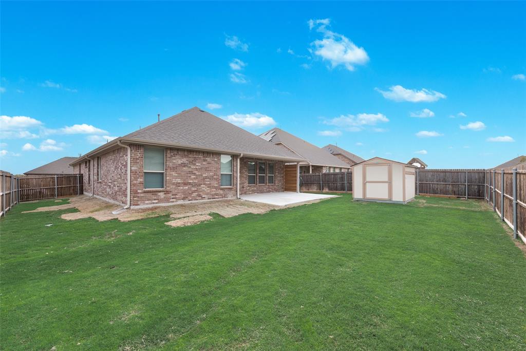 1419 Fox Hollow Road Krum, TX 76249 - Photo 25 of 29 Rear view of property featuring a fenced backyard, a patio area, brick siding, a storage unit, and roof with shingles