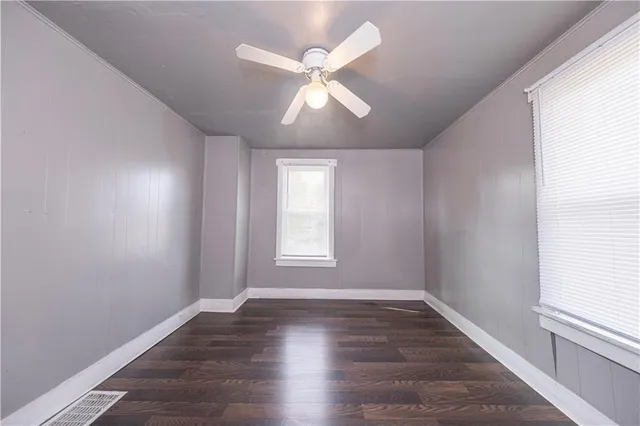 an empty room with wooden floor windows and fan
