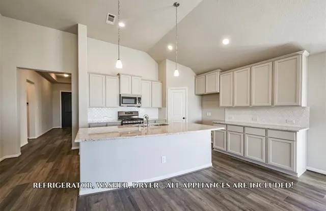 a large kitchen with stainless steel appliances kitchen island granite countertop a stove a sink a refrigerator and white cabinets with wooden floor