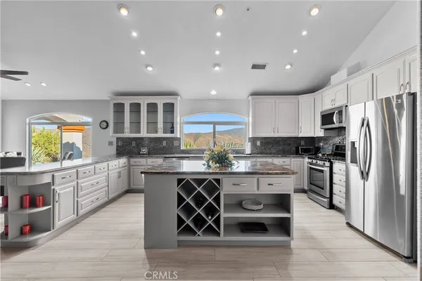 a kitchen with stainless steel appliances granite countertop a stove a sink dishwasher a refrigerator and white cabinets with wooden floor
