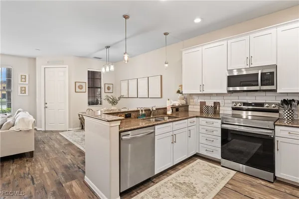 a kitchen with stainless steel appliances granite countertop a stove top oven a sink dishwasher and a refrigerator with wooden floor