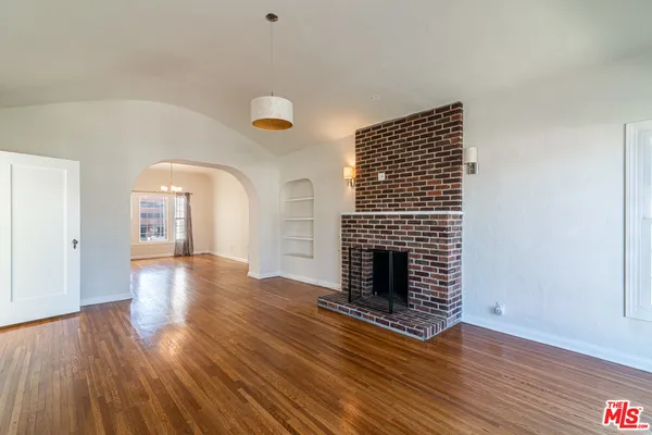 a view of an empty room with wooden floor fireplace and a window