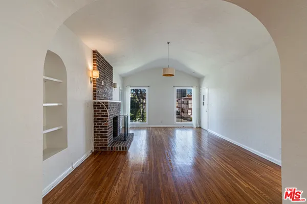 an empty room with wooden floor fireplace and windows