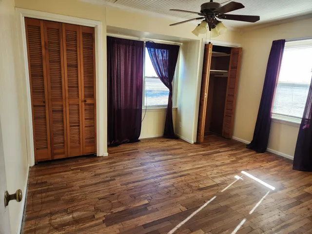 an empty room with wooden floor fan and windows