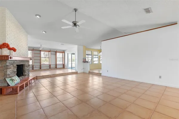 a view of an empty room with chandelier fan and fire place