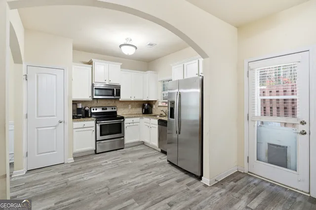 a kitchen with granite countertop white cabinets appliances a sink and a window