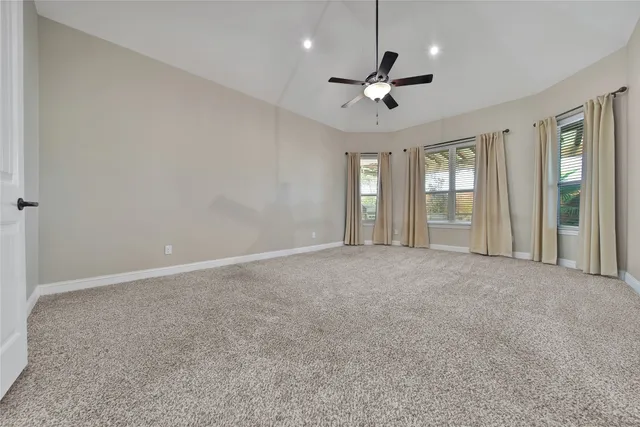 an empty room with chandelier fan and windows