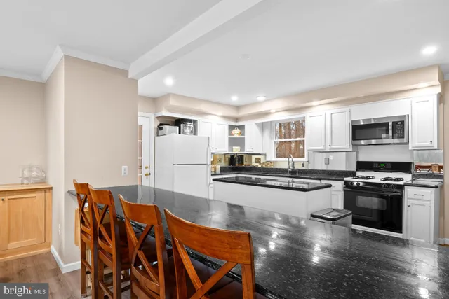 a kitchen with stainless steel appliances granite countertop a stove top oven a sink a dining table and chairs with wooden floor