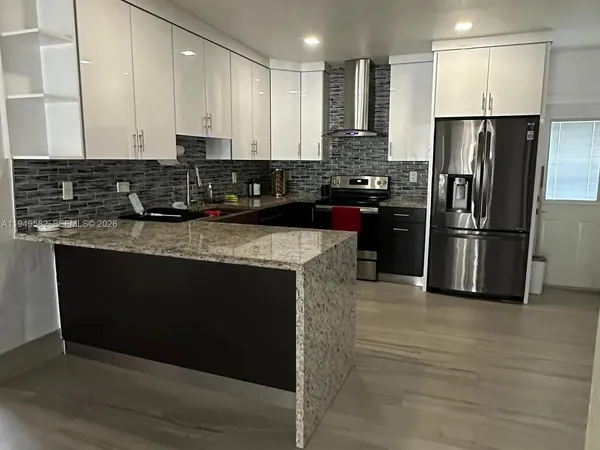a kitchen with stainless steel appliances granite countertop a stove a sink dishwasher a refrigerator and white cabinets with wooden floor