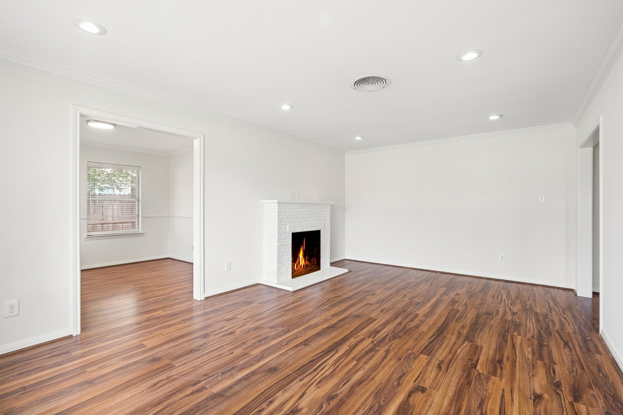 3331 Arbor Street Houston, TX 77004 - Photo 5 of 30 This room features a spacious layout with warm wood flooring and a white brick fireplace, creating a cozy ambiance. Recessed lighting enhances the modern, clean look, and an adjacent room is visible through an open doorway, offering flexibility for use.