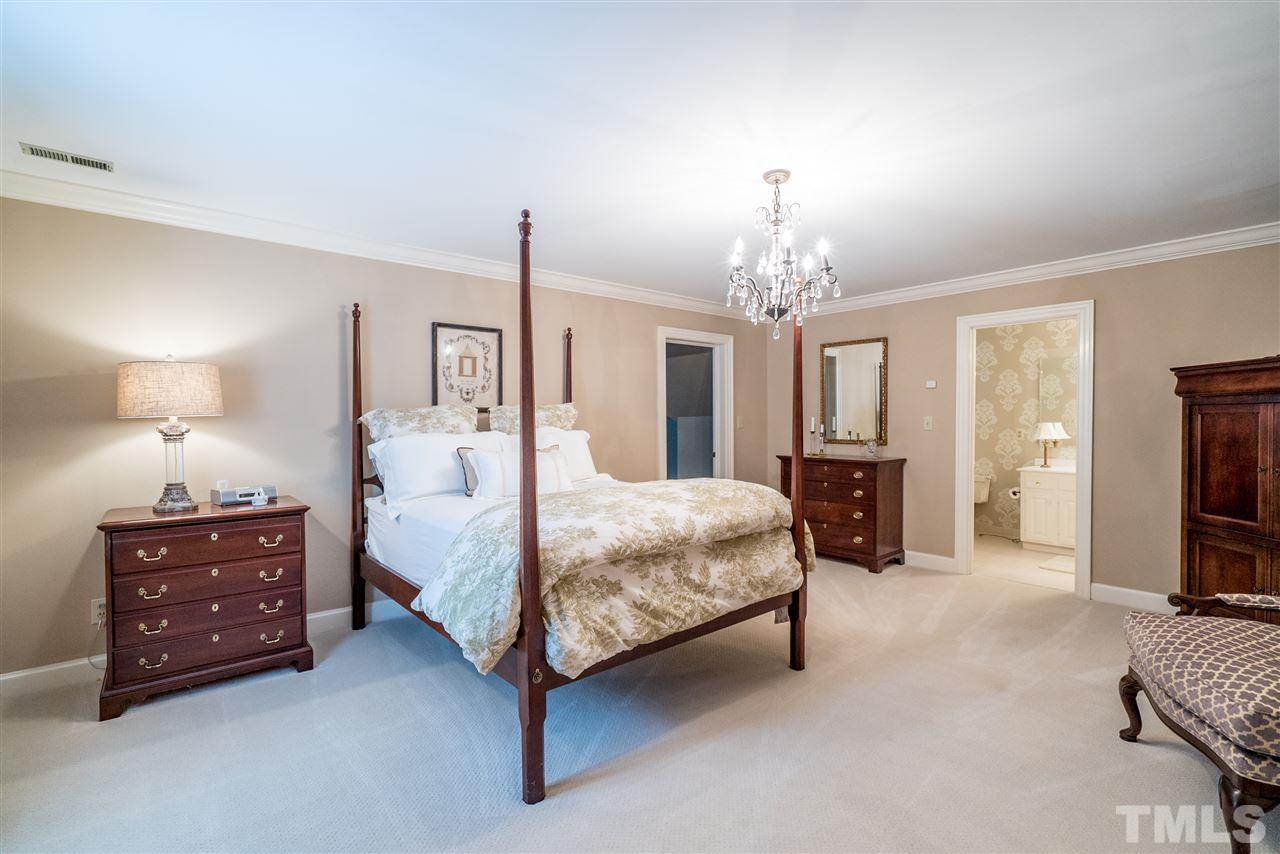 9904 Mathias Court Raleigh, NC 27615 - Photo 16 of 25 a spacious bedroom with a bed a mirror on dresser and a chandelier
