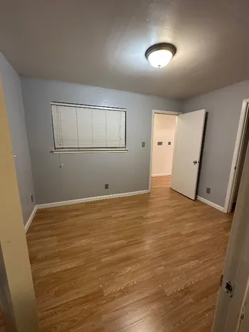 a view of an empty room with wooden floor and a ceiling fan
