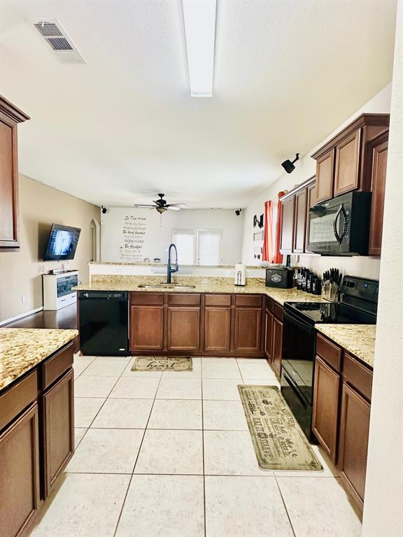 111 Rebel Road Venus, TX 76084 - Photo 4 of 7 Spacious kitchen featuring extensive brown cabinetry, black appliances, light-colored tile flooring, and granite countertops