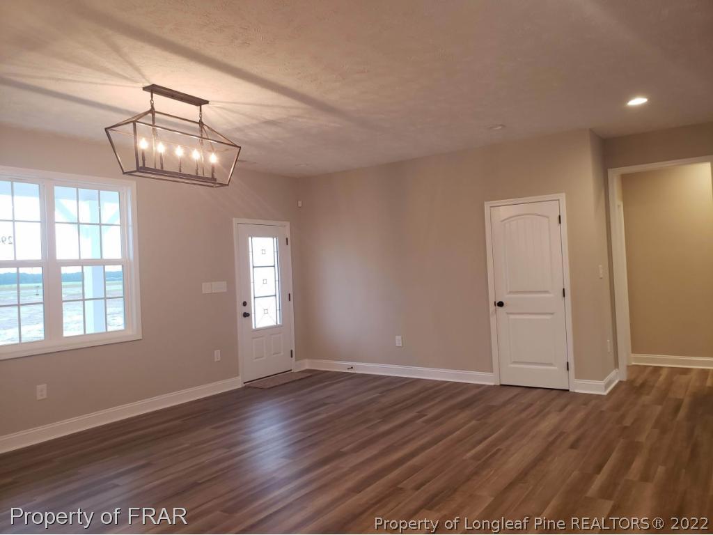 2945 Hayfield Road Wade, NC 28395 - Photo 4 of 26 an empty room with wooden floor chandelier and windows