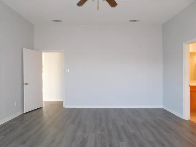 an empty room with wooden floor fan and windows
