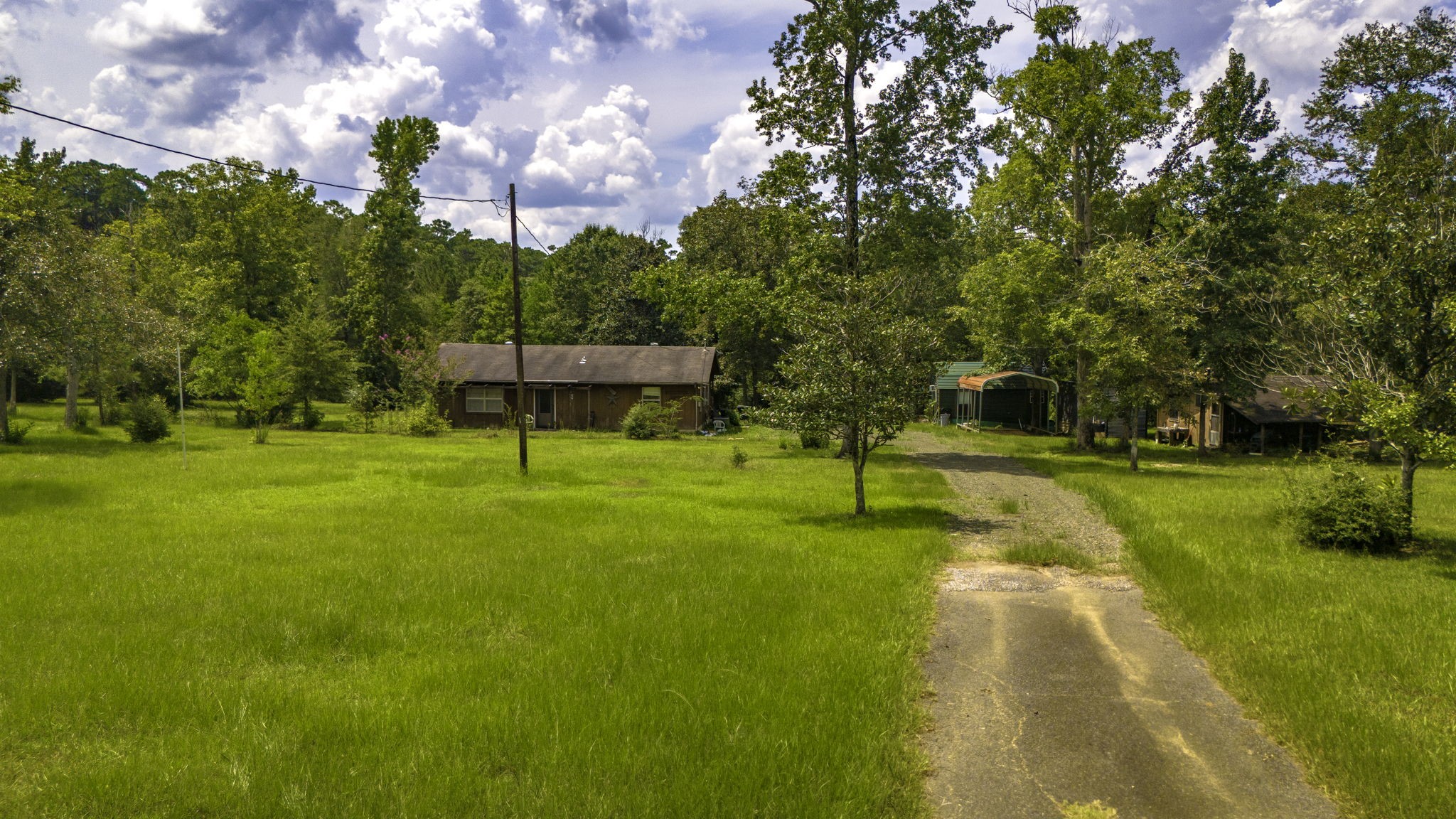 This photo shows a rustic home set in a spacious, grassy lot surrounded by trees. A driveway leads up to the house, offering a peaceful, rural atmosphere.