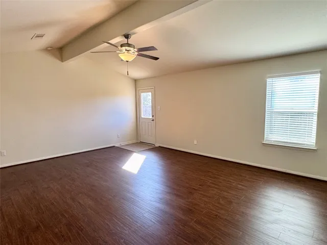 an empty room with wooden floor chandelier fan and windows