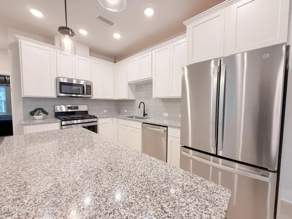 a kitchen with granite countertop a refrigerator a sink a stove and cabinets