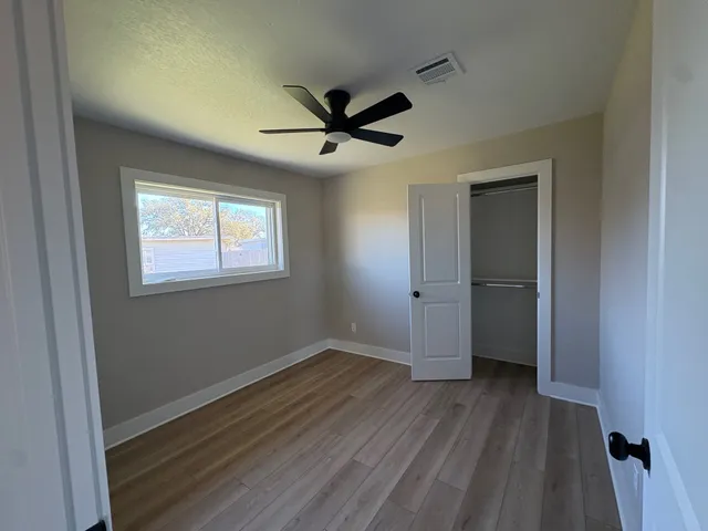 a view of a livingroom with wooden floor a ceiling fan and windows