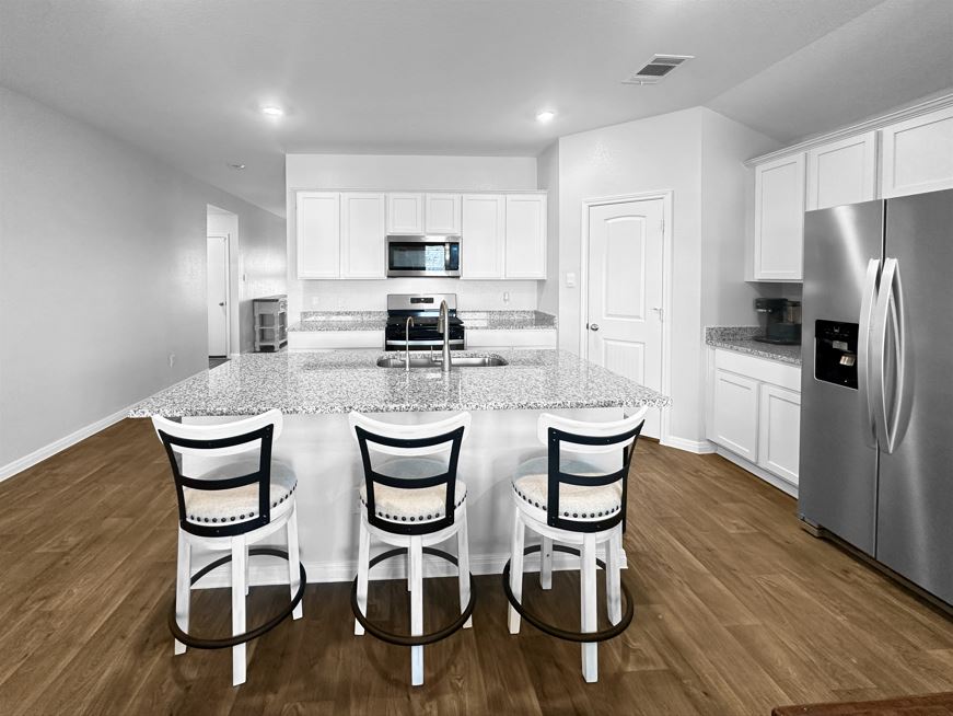 730 Gladiola Loop Kyle, TX 78640 - Photo 4 of 13 Kitchen featuring white cabinetry, stainless steel appliances, an island with sink, dark wood-style floors, and recessed lighting