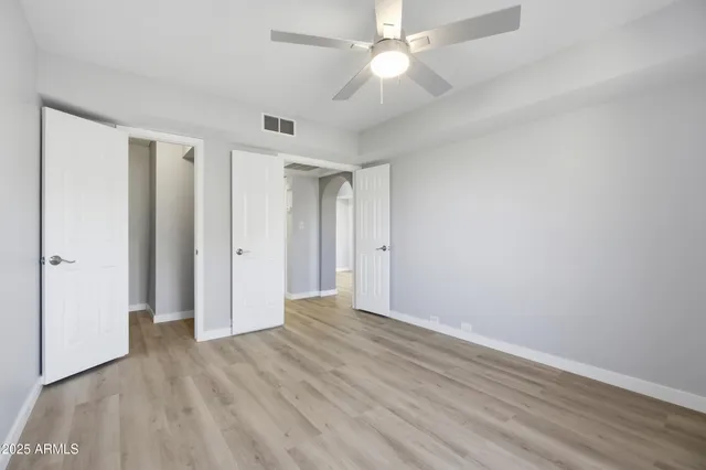 an empty room with wooden floor fan and windows