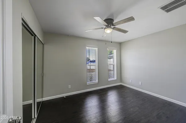 an empty room with wooden floor chandelier fan and windows
