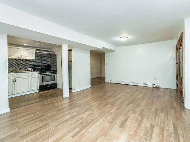 an empty room with wooden floor a kitchen view and windows