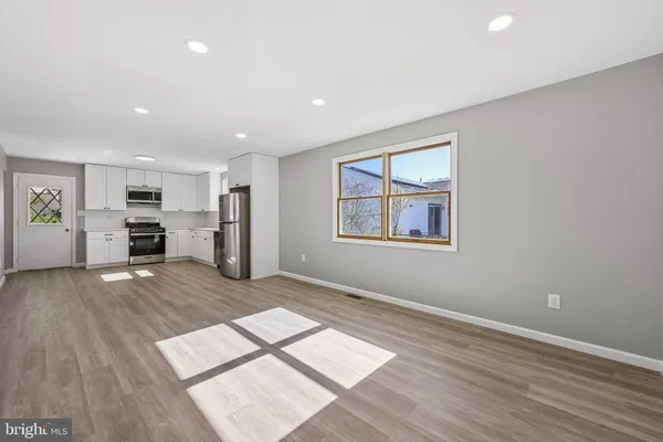an empty room with wooden floor kitchen view and windows