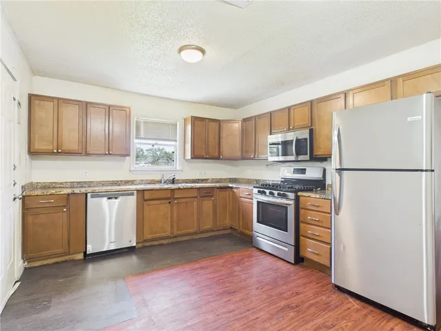 a kitchen with stainless steel appliances granite countertop a refrigerator a stove top oven a sink and dishwasher with wooden floor