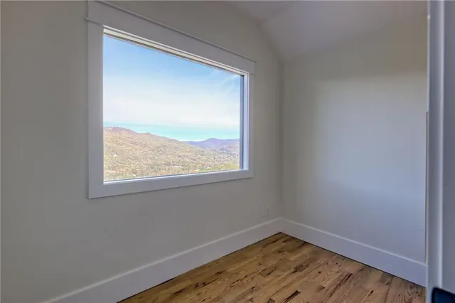 a view of an empty room with wooden floor fireplace and a window
