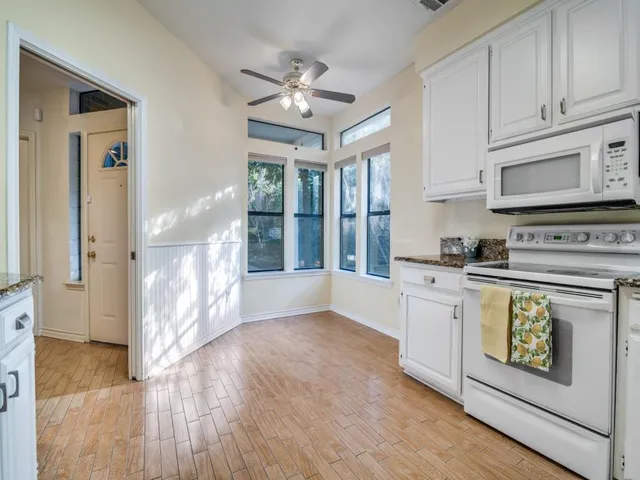 a kitchen with stainless steel appliances granite countertop a stove top oven a refrigerator a sink and white cabinets with wooden floor