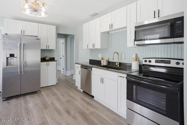 a kitchen with stainless steel appliances a refrigerator a stove a dining table and chairs with wooden floor