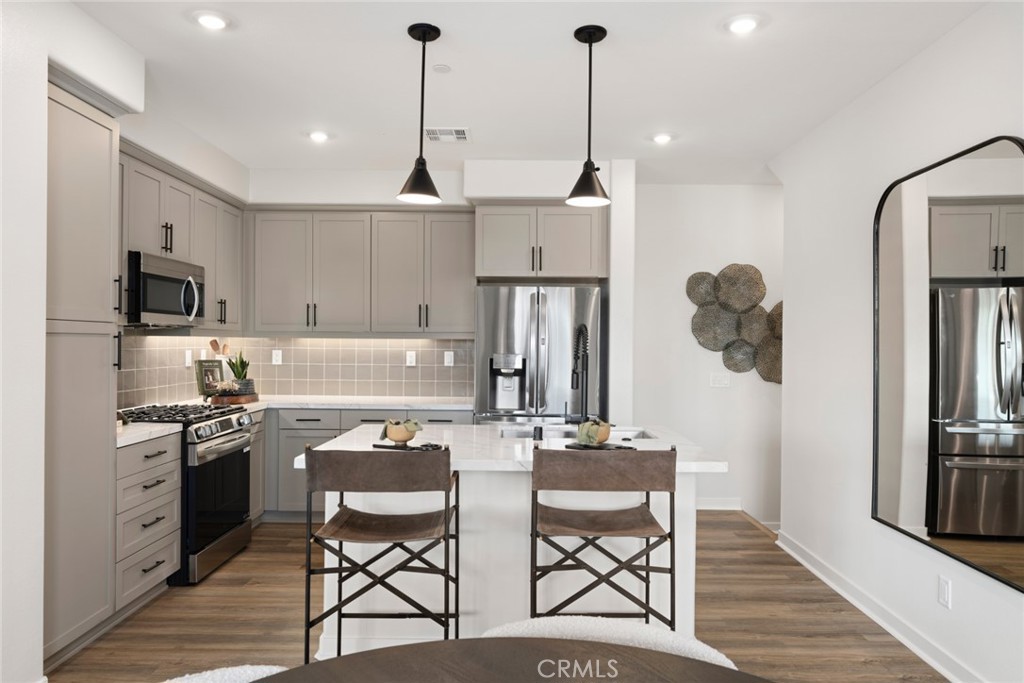 12250 Mirasol Loop, Unit H El Monte, CA 91732 - Photo 7 of 18 a kitchen with stainless steel appliances granite countertop a stove a refrigerator and a dining table with wooden floor